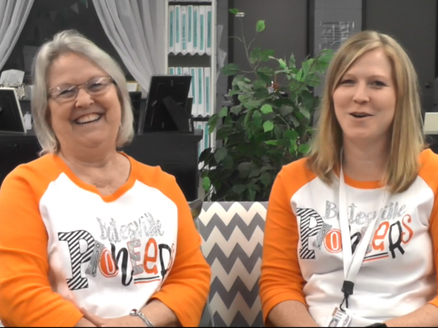 Two women, a mother and daughter, wear orange and white t-shirts and sit on a couch with gray, zigzag stripes.